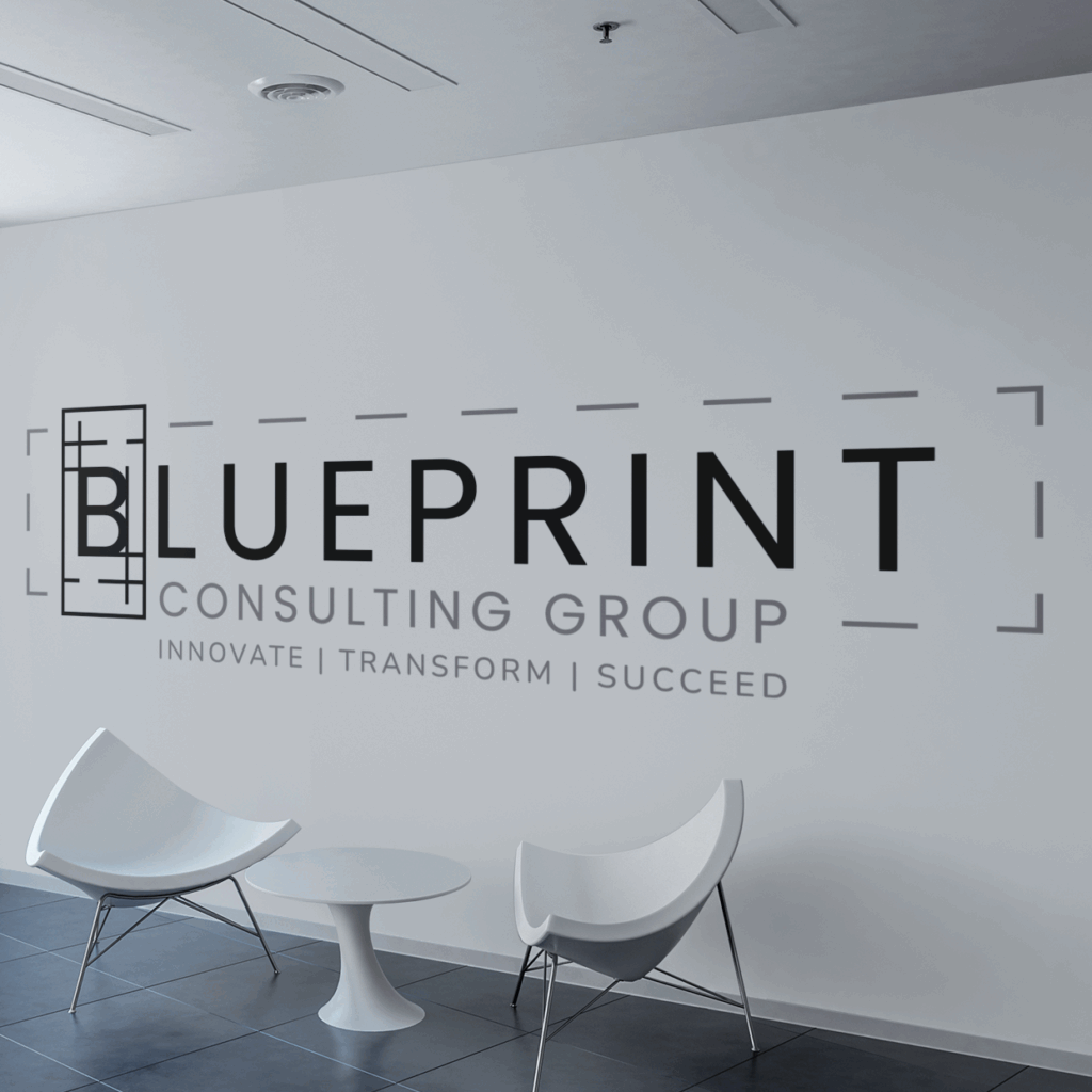 A modern office wall in consulting group Raleigh NC displays the logo for BLUEPRINT CONSULTING GROUP with the tagline INNOVATE | TRANSFORM | SUCCEED above two white chairs and a small round table.