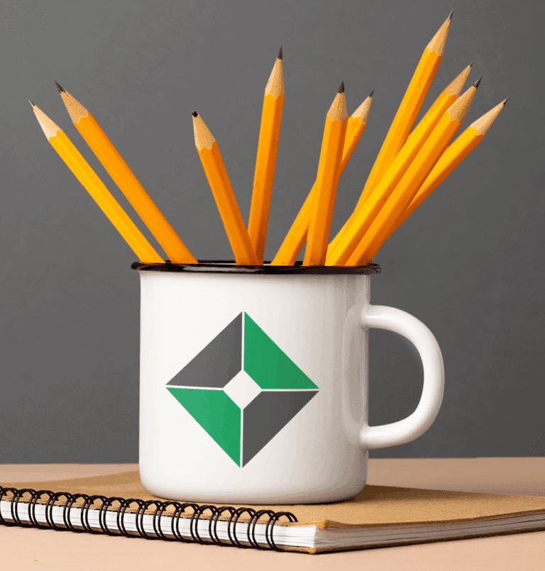 A white mug with a green and black geometric logo—perfect for showcasing your Logo Design skills—holds sharpened yellow pencils. The mug rests on a spiral notebook with a brown cover, set against a plain gray background.