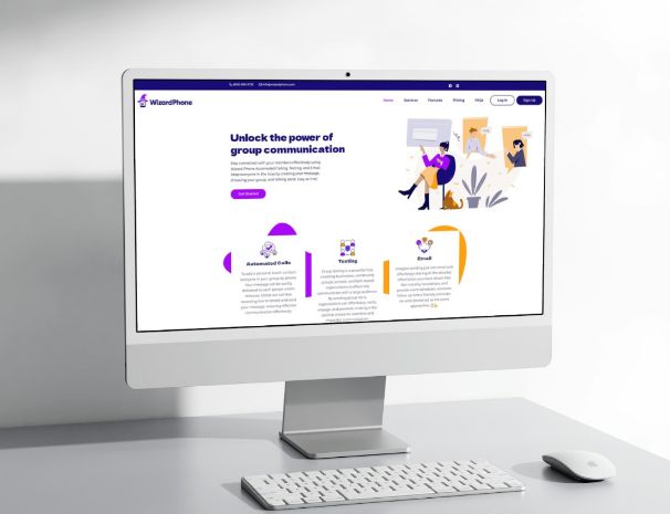 A computer monitor on a white desk displays a website design with the heading Unlock the power of group communication, colorful icons, and illustrations of people interacting. A keyboard and mouse are also on the desk.