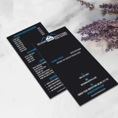 Two black business cards for Diligent Home Inspections are displayed on a white surface, with purple flowers in the background. Showcasing strong branding, the cards list contact details, services, and website design support in blue and white text.