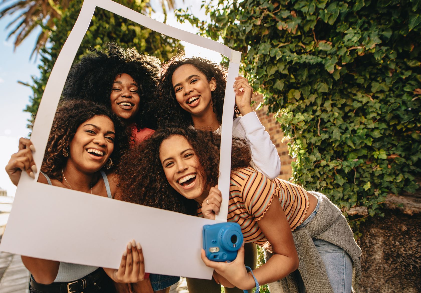 Four young women joyfully holding a photo frame, symbolizing teamwork and collaboration in achieving business goals.