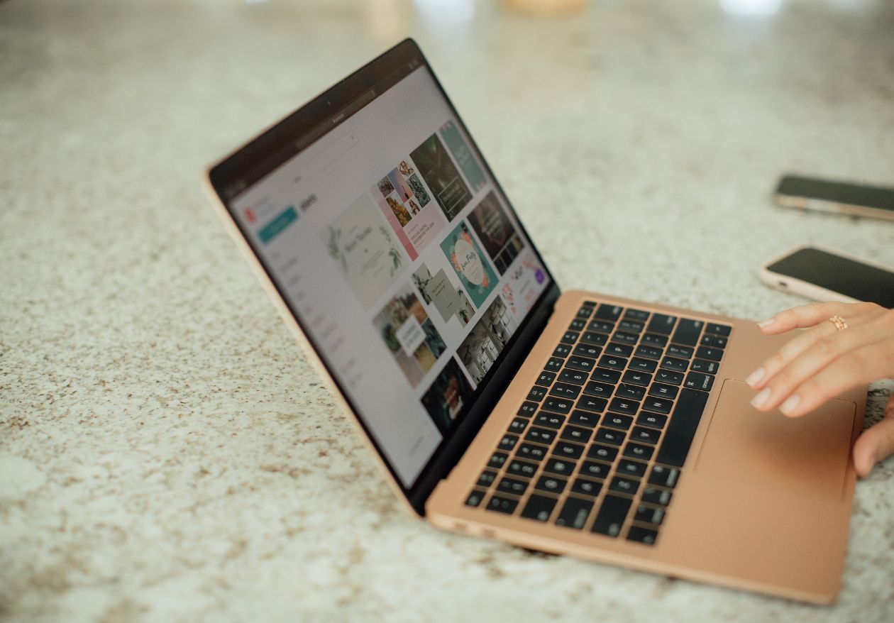 Individual working on a laptop at a table, utilizing design software like Canva or Adobe Spark for projects.