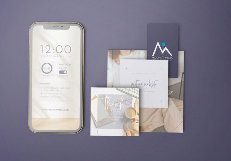 A smartphone displaying a minimalist calendar screen sits beside assorted business cards and thank you notes on a purple surface, with one card showcasing the Moonlit Media logo—highlighting their expertise in custom website design.
