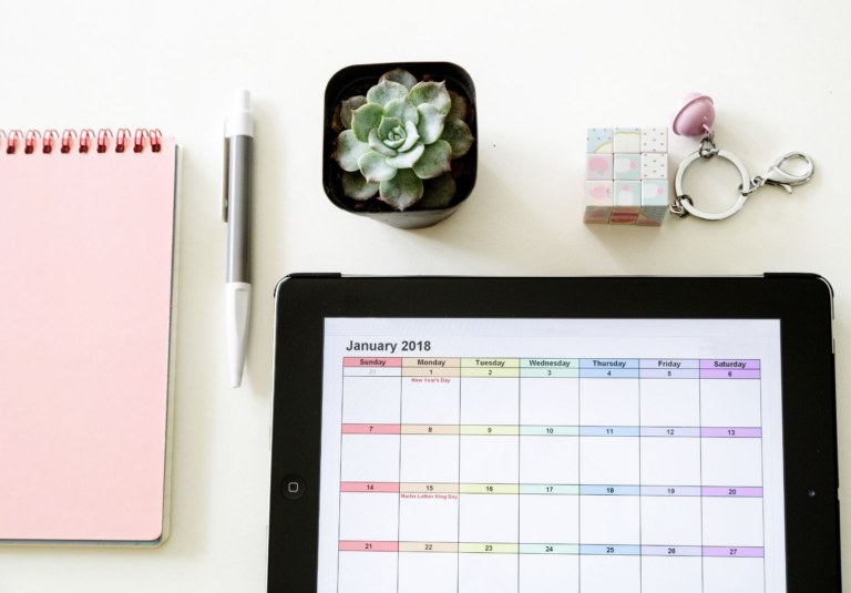 A flat lay of a pink notebook, pen, potted succulent, Rubik’s cube keychain, and a tablet displaying a January 2018 calendar—all perfectly arranged like a web designer planning custom website design on a clean white surface.