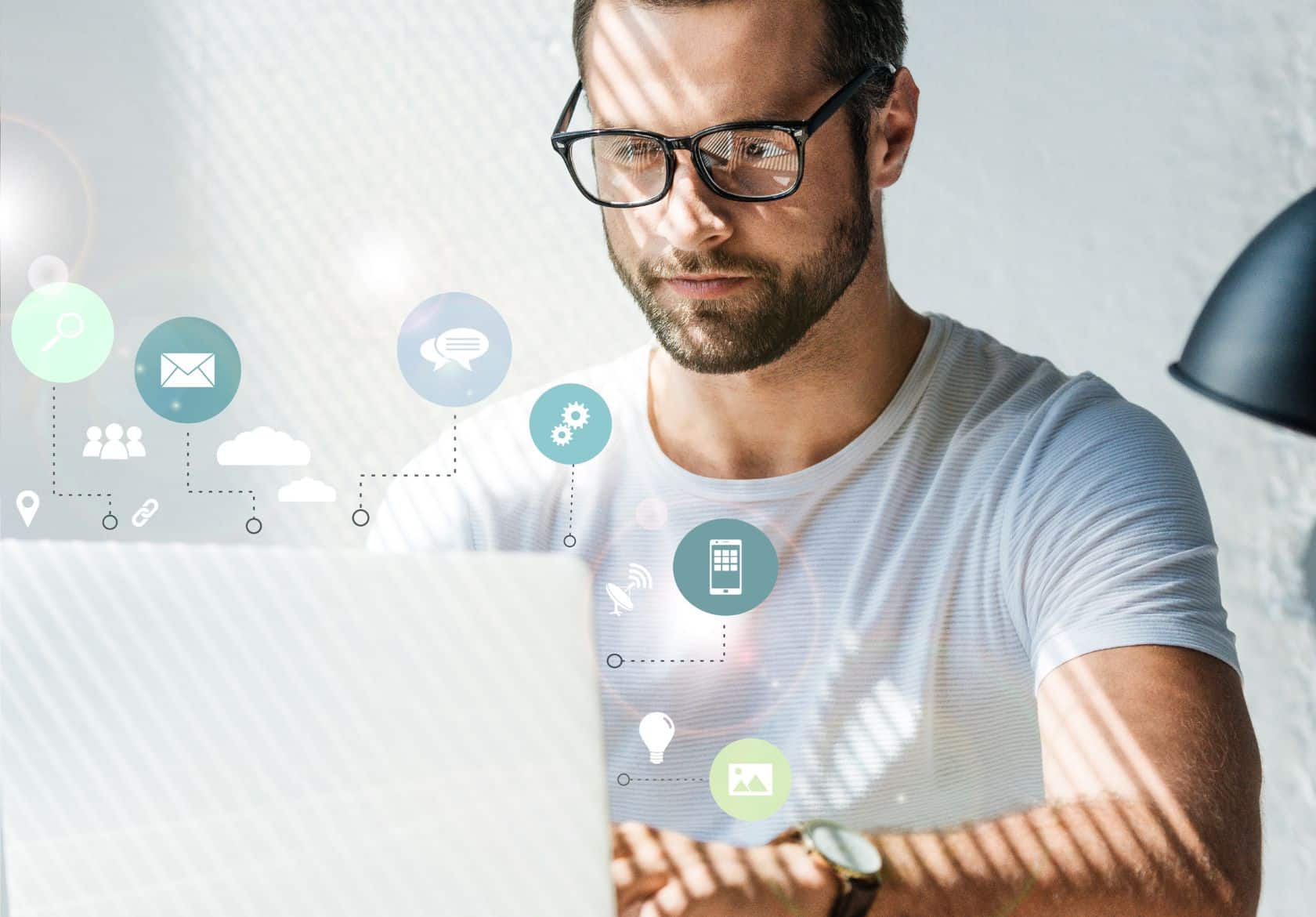 A man wearing glasses and a white shirt works on a laptop, with sunlight casting shadows on him. Floating digital icons for cloud computing, email, and communication hint at custom website design and advanced web design services near the screen.