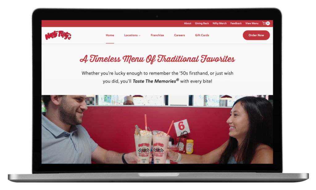 Nifty Fiftys Restaurant | Moonlit Media LLC A laptop screen displays the Nifty Fiftys website for its New Hampshire diner, showing a smiling man and woman clinking milkshakes at a table. The site headline reads, A Timeless Menu Of Traditional Favorites, highlighting their recent website redesign.