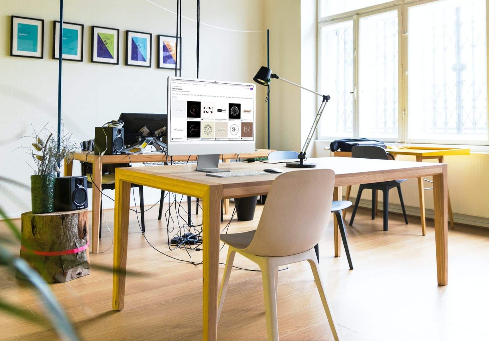 Bright modern office with wooden desks, chairs, and a desktop computer—perfect for a web designer or custom logo design work. Sunlight streams through large windows; a tree stump with a vase and speakers adds Moonlit Media flair to the corner.