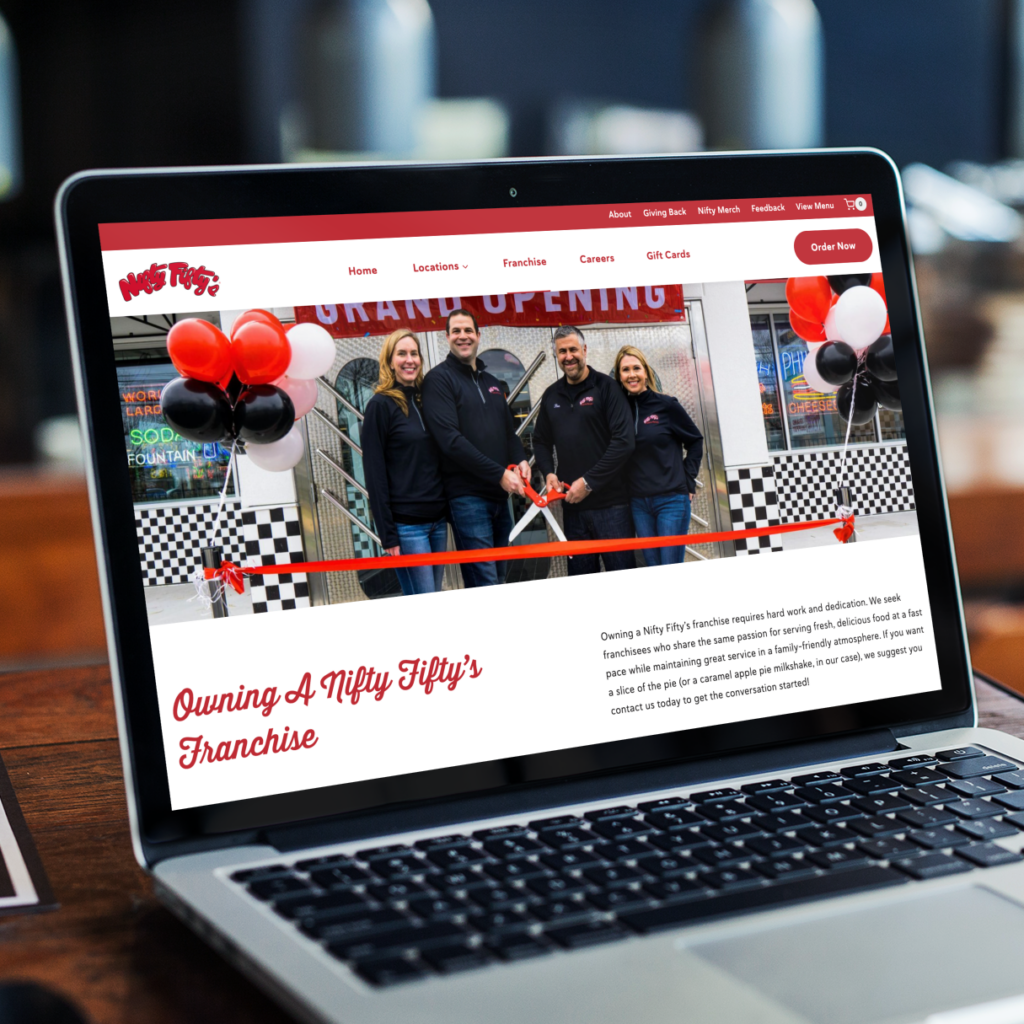 A laptop screen displays Nifty Fifty’s website redesign, showing four people at a grand opening with balloons, a ribbon, and large scissors. The site features franchise info, New Hampshire locations, and a red Order Now button.