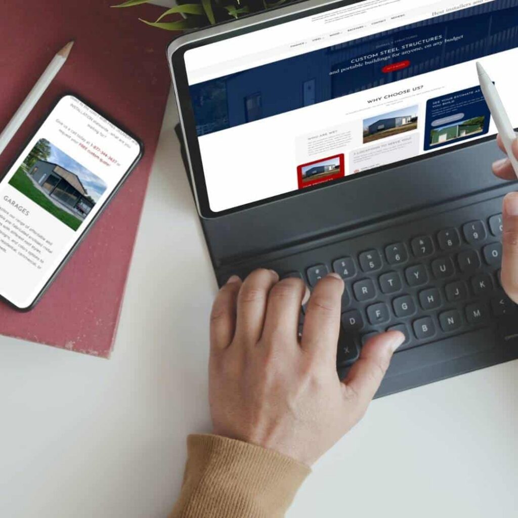 A web designer uses a stylus on a tablet with a keyboard while browsing a website; nearby, a smartphone displays an image of a building and text about garages, showcasing moonlit media’s custom website design.