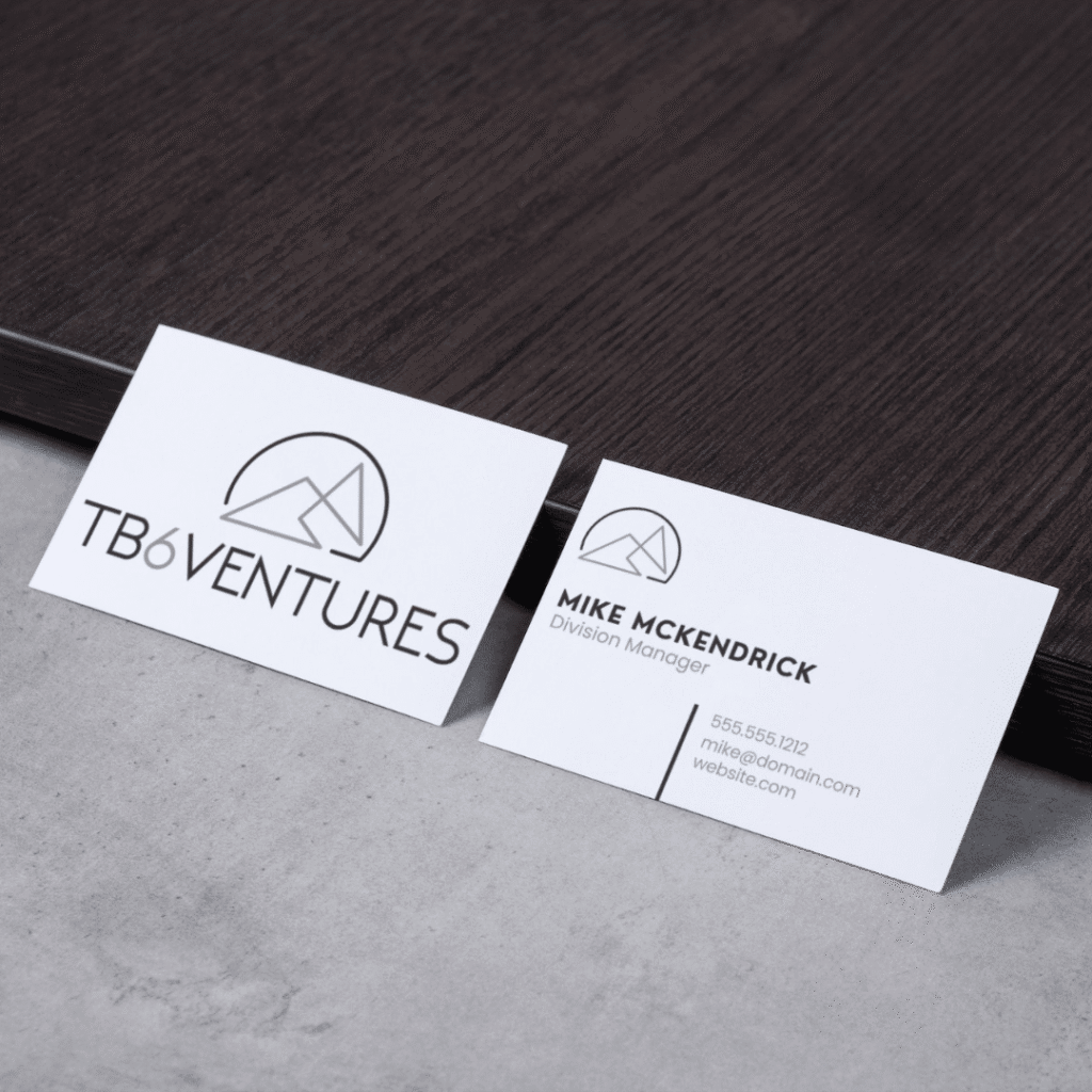 Two business cards on a table, one featuring the TB6 Ventures logo designed by Moonlit Media and the other displaying contact details for Mike McKendrick, Division Manager, with a matching custom logo design in the corner.