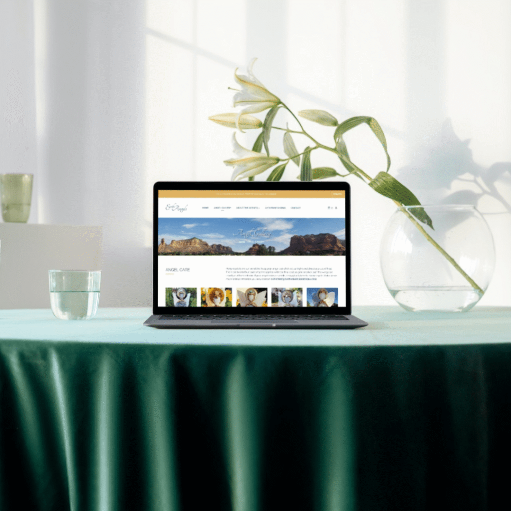 A laptop displaying a website sits on a green tablecloth, suggesting web design services. Nearby are a glass of water, a large vase with water, and a white lily in a tall green vase, all bathed in soft natural light.