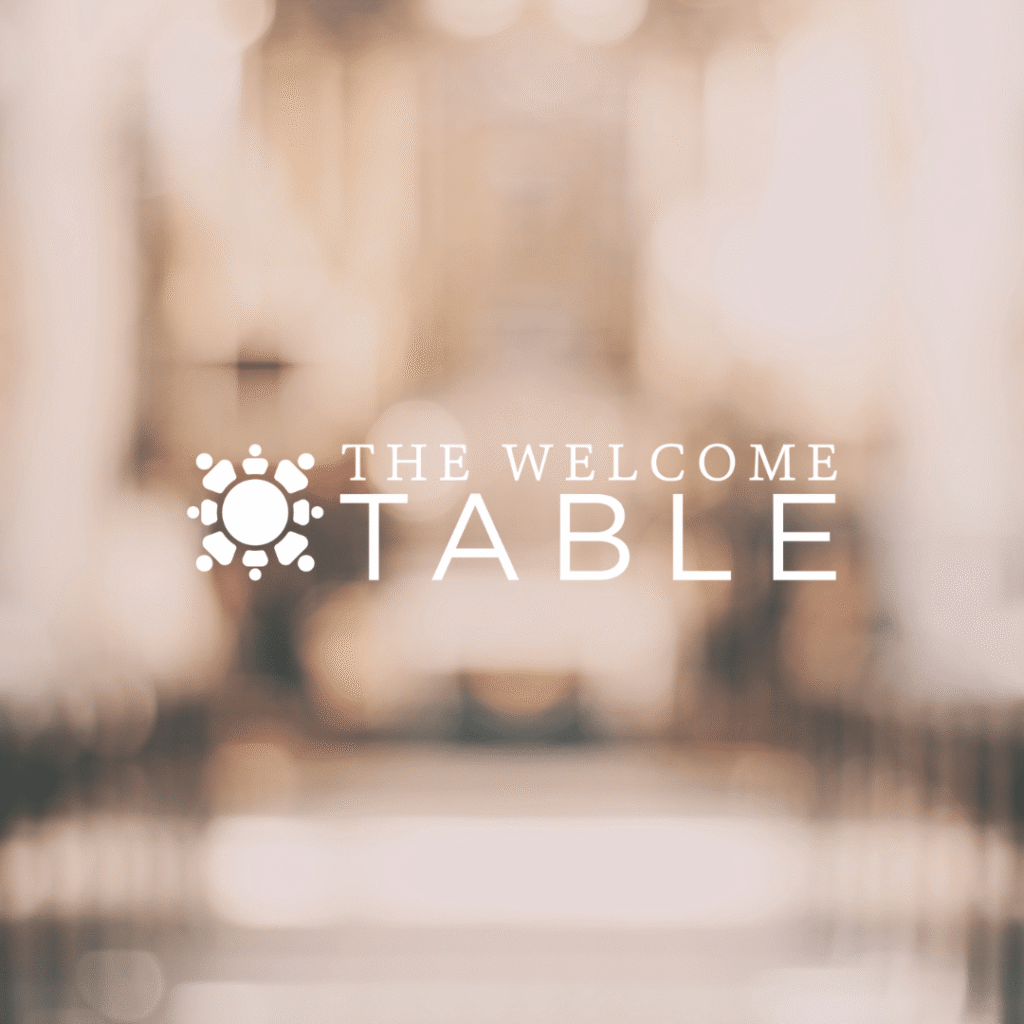 White text reading The Welcome Table is centered on a blurred, warm-toned background. A round table icon evokes gathering and inclusion—perfect inspiration for web designers seeking custom logo design ideas.