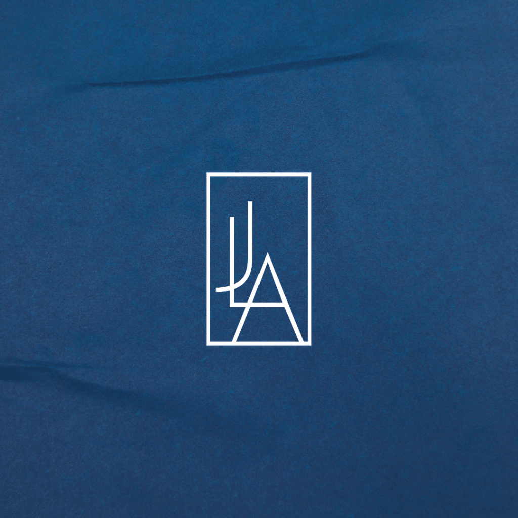A white geometric logo with overlapping stylized letters JLA inside a rectangle, centered on a textured blue background—perfect for any web designer seeking custom logo design inspiration from Moonlit Media.