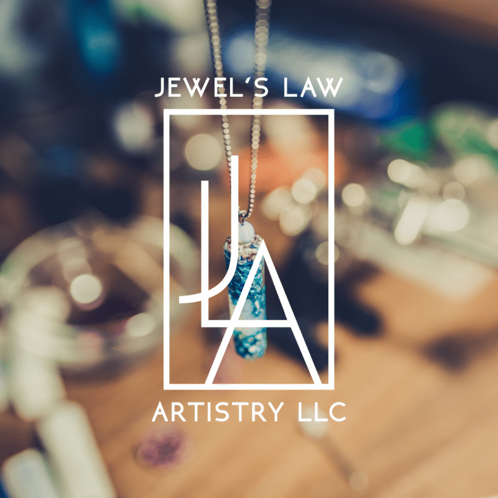 A close-up of a blue pendant necklace on a chain, with a blurred background of jewelry-making tools. Overlaid text reads: Jewels Law Artistry LLC with a stylized logo, showcasing custom website design by Moonlit Media.