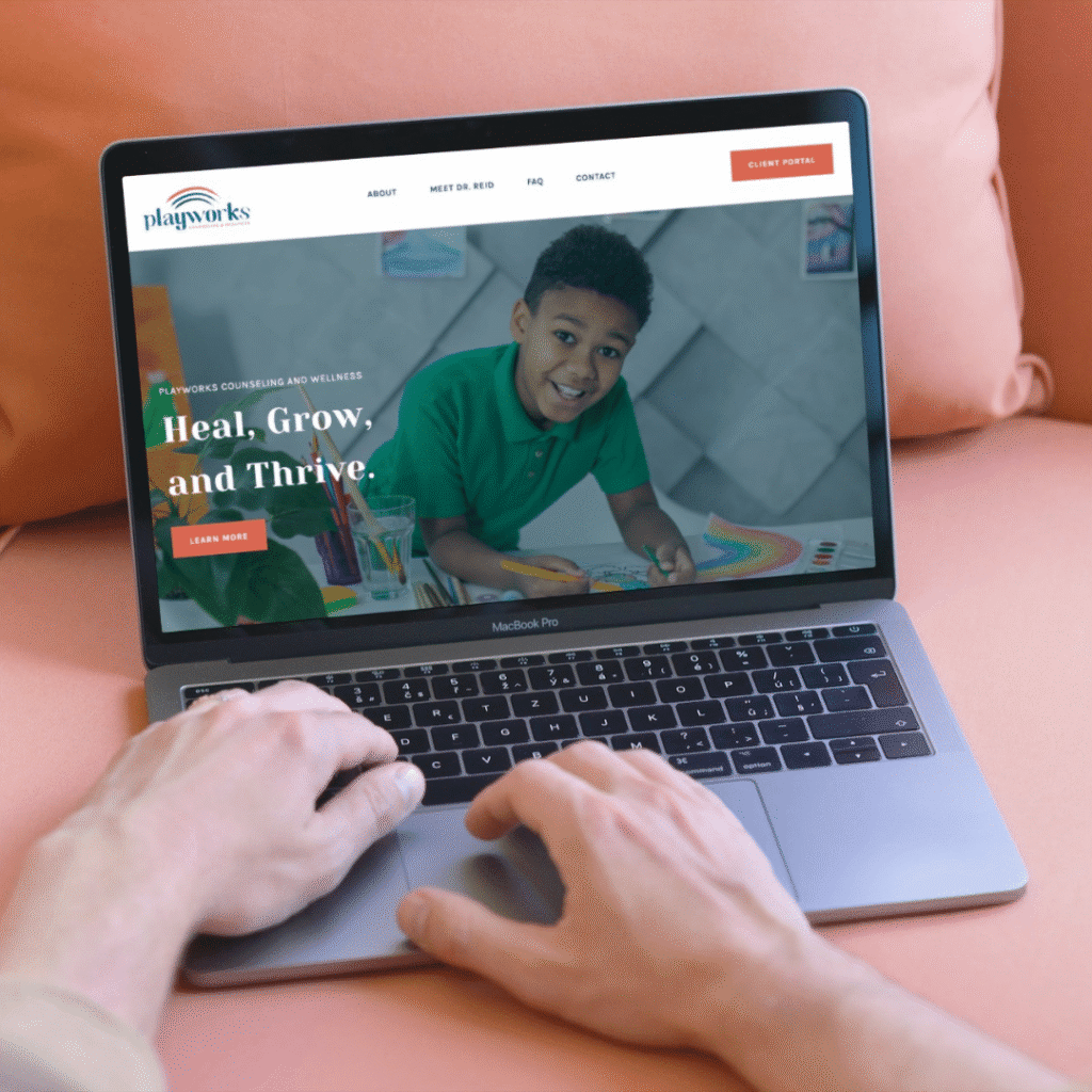 A person uses a MacBook Pro on a peach-colored couch, viewing a custom website design featuring a smiling child drawing and the text Heal, Grow, and Thrive. The site header reads Playworks Counseling and Wellness.