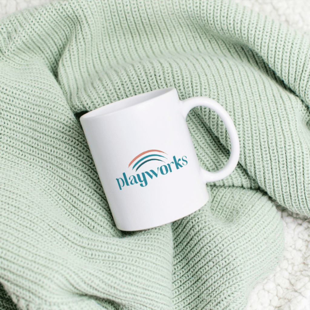 A white mug with the “playworks” logo sits on a light green knitted blanket, highlighting the impact of thoughtful logo design services.