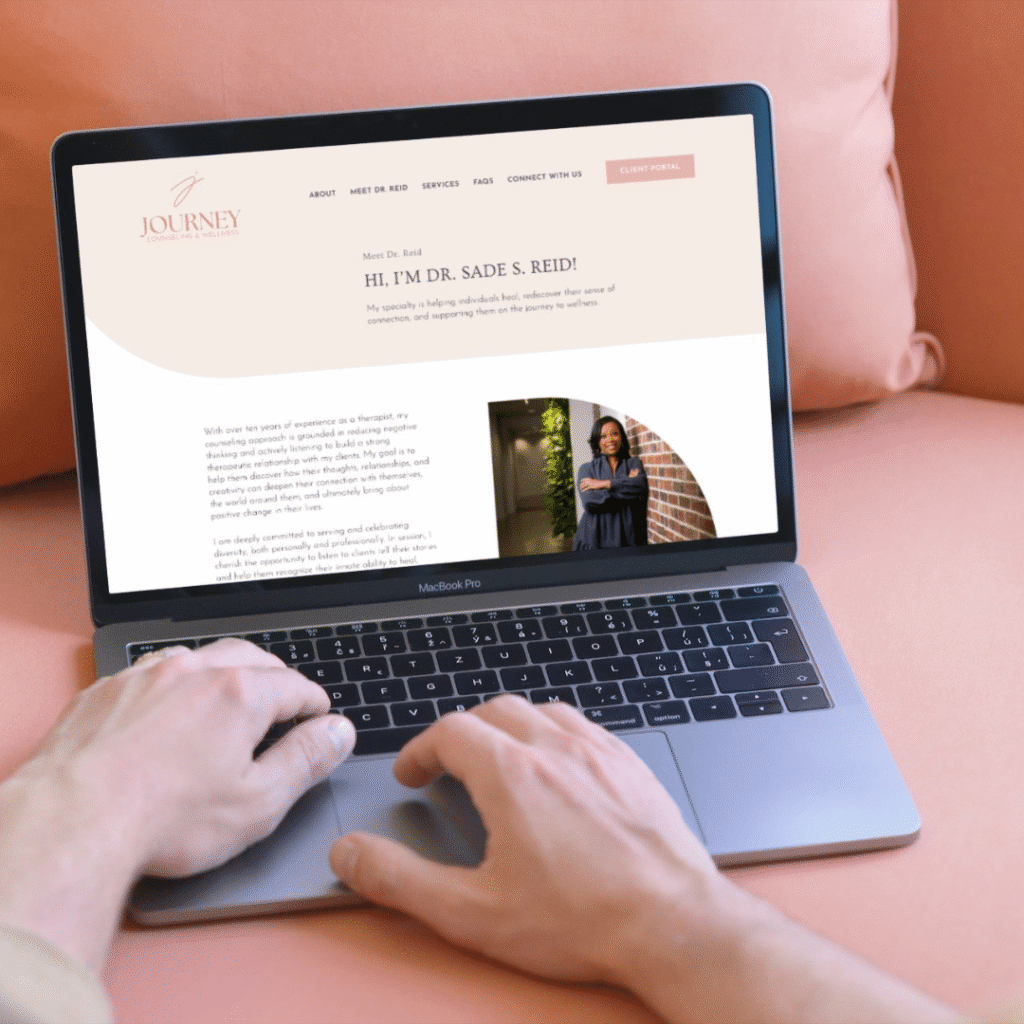 210 | Moonlit Media LLC A person types on a MacBook Pro laptop displaying Dr. Sade S. Reid’s website, featuring her photo, a welcome message, and info about web design services, while sitting on a pink couch.