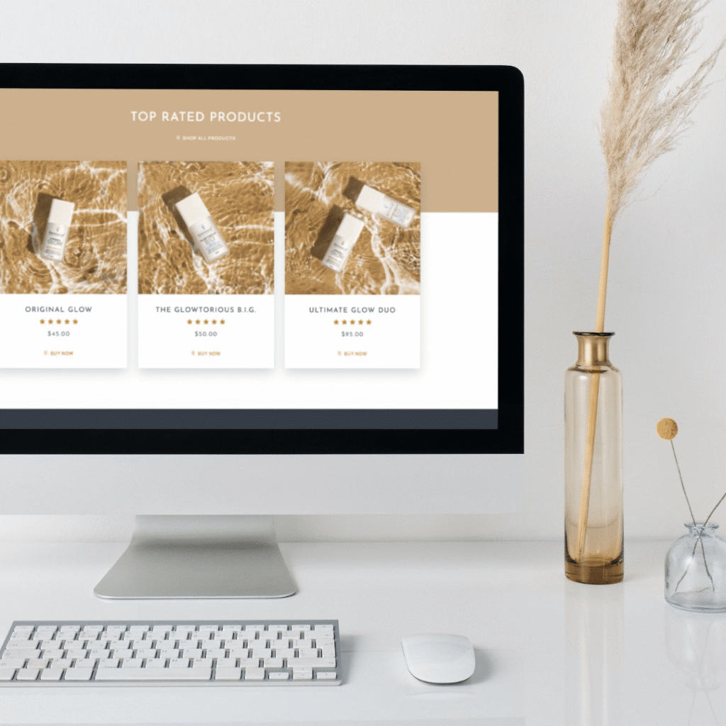 A desktop computer on a white desk displays a custom website design featuring top-rated skincare products. A keyboard, mouse, notebook, and a tall vase with dried grass are also on the desk.