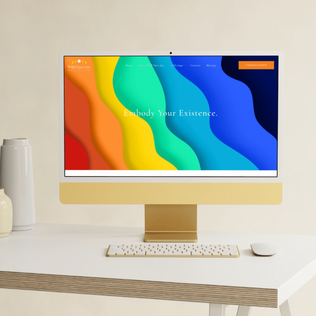 A desktop computer on a white desk displays a custom website design with wavy rainbow patterns and the text Embody Your Existence. A wireless mouse, keyboard, and two vases complete the stylish setup.