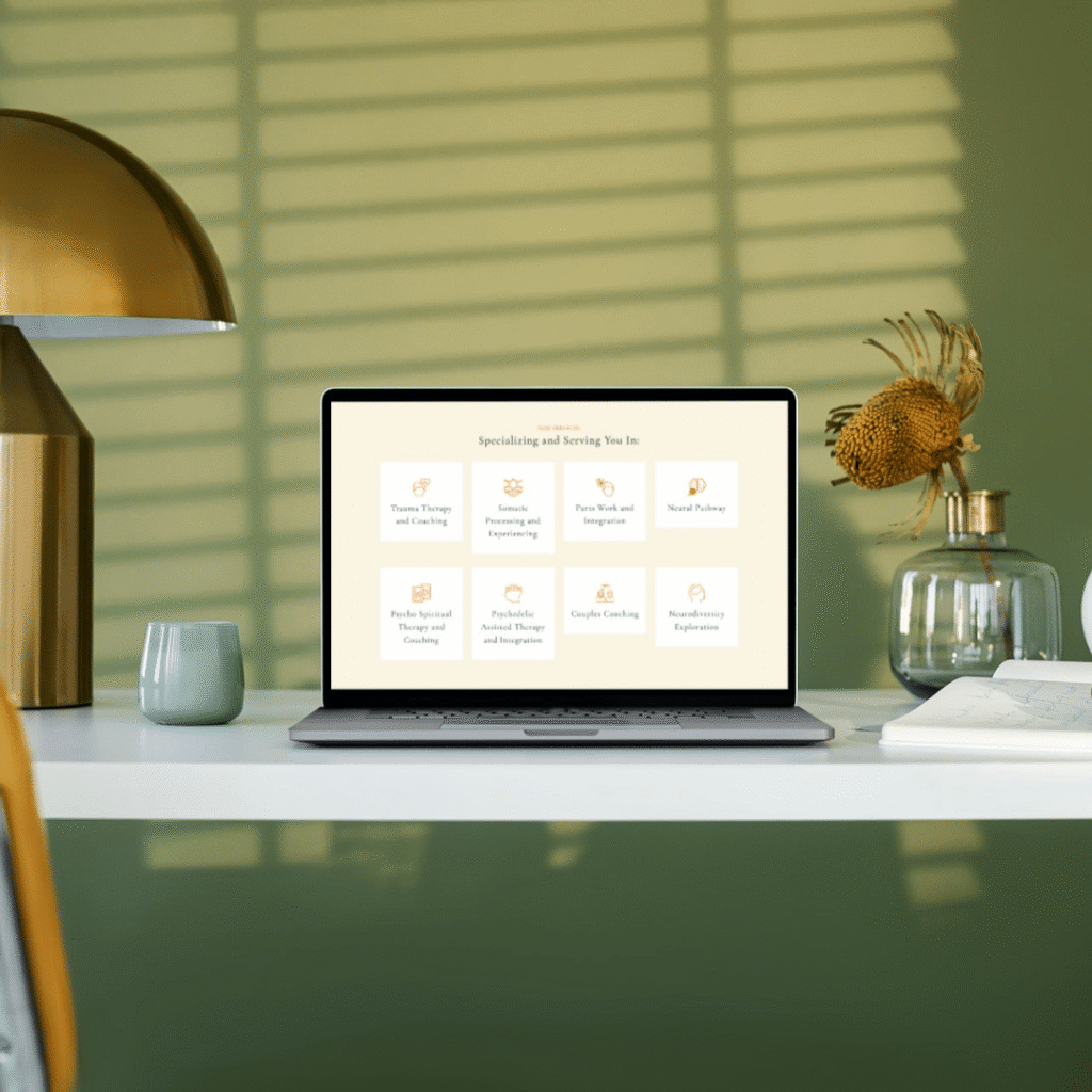 A laptop sits on a white desk with a modern lamp, flower, and green wall. The screen displays a grid of services from Moonlit Media, including therapy, coaching, custom website design, and workshops. Sunlight casts shadows across the scene.
