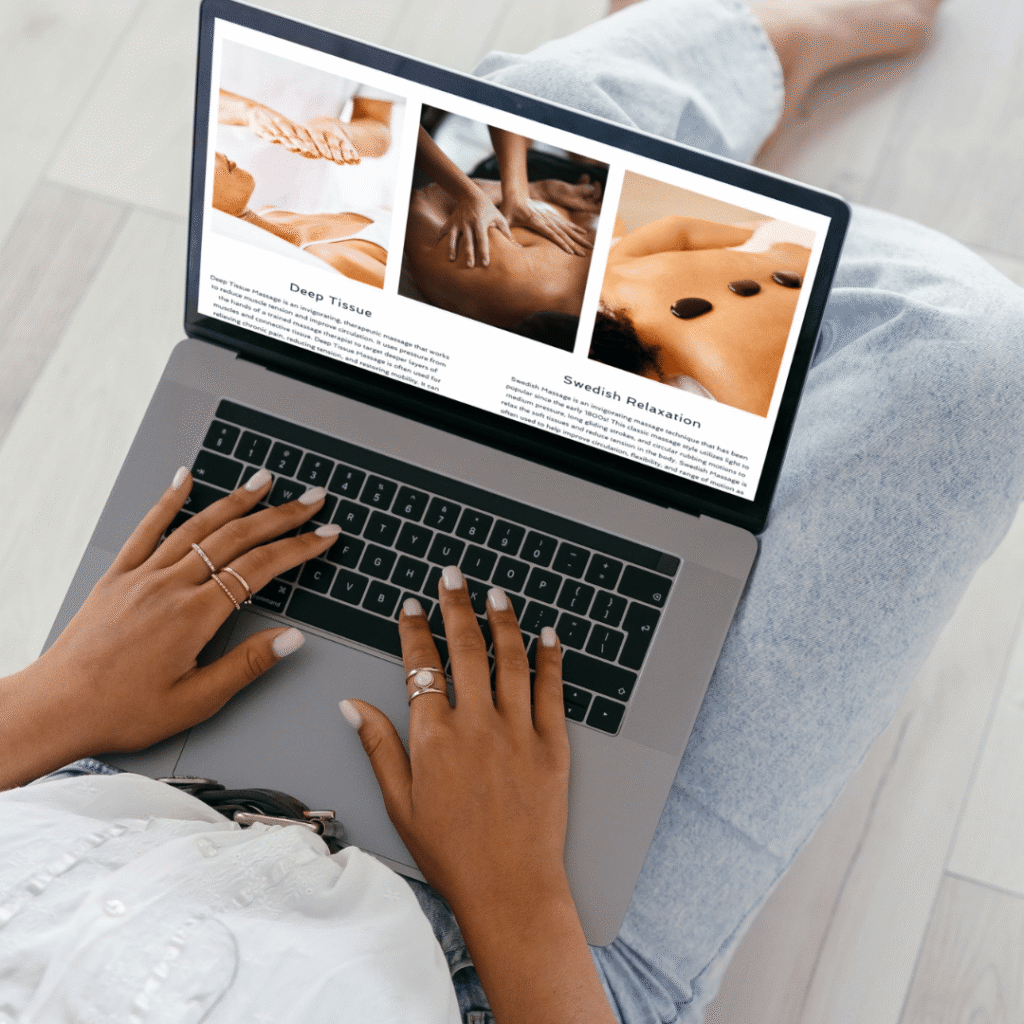 A person sitting on the floor in jeans uses a laptop, viewing a webpage with images of massages and descriptions of different massage techniques, exploring custom website design for spa businesses.