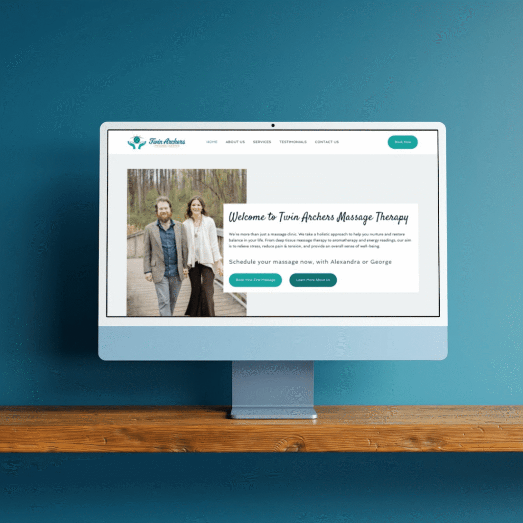 A computer monitor displays the Twin Arches Massage Therapy website, designed by Moonlit Media, featuring a photo of a smiling man and woman walking in a wooded area, with navigation links and welcome text on a blue desk against a blue wall.