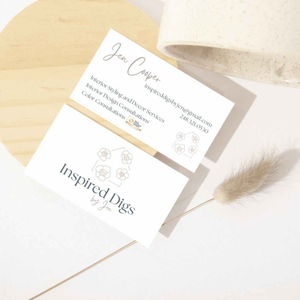 Two business cards for Inspired Digs by Jen are displayed on a light wooden surface, featuring floral line art and contact details for Jen Cooper, with a nod to moonlit media’s custom logo design in the minimalist decor background.