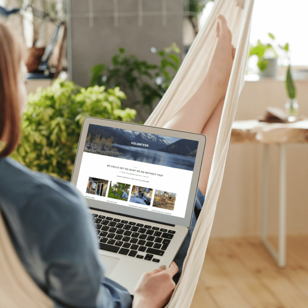 A person sits in a hammock at home, using a laptop displaying a custom website design for a volunteer site. There are green plants and sunlight in the background, creating a relaxing atmosphere.