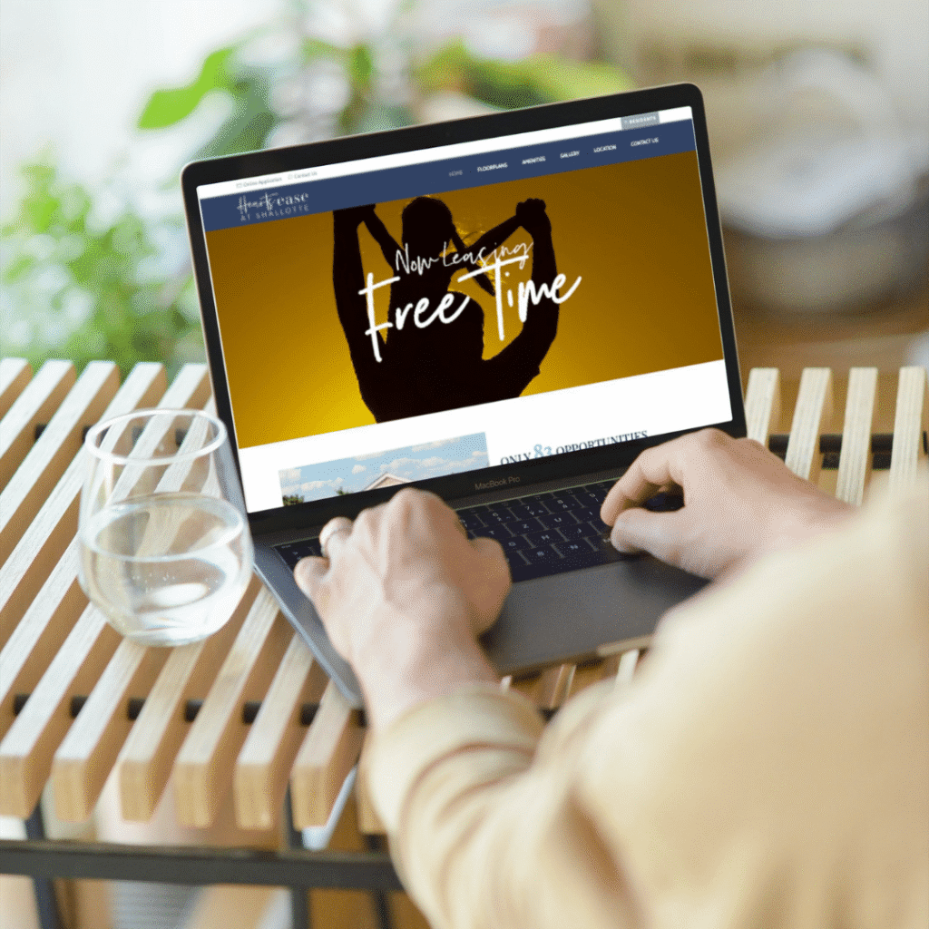 Person using a laptop on a wooden table, viewing a website about free time with a silhouette celebrating. A glass of water sits nearby—an inspiring scene for any web designer or those interested in creative web design services.