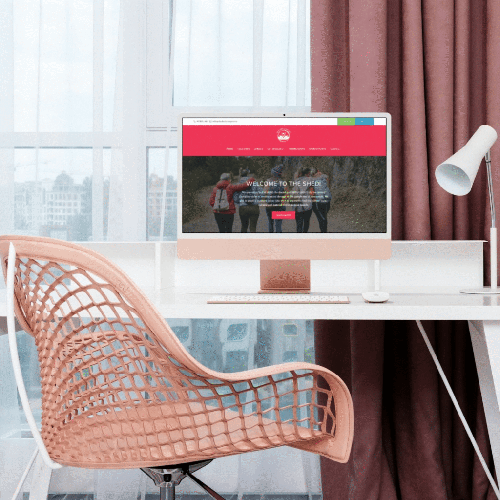 27 | Moonlit Media LLC A modern workspace with a pink mesh chair, a white desk, and a computer displaying custom website design by Moonlit Media. Pink curtains hang by a large window with a city view in the background.