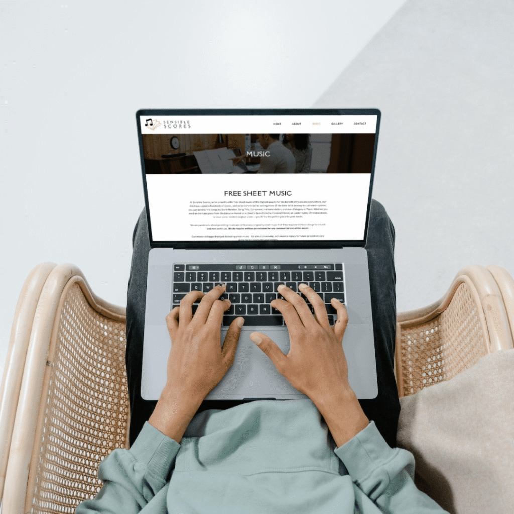 A person sits in a wicker chair using a laptop on their lap, viewing a website that offers free sheet music. Their hands are on the keyboard, and the photo, taken from above, suggests a web designer browsing for inspiration from Moonlit Media.