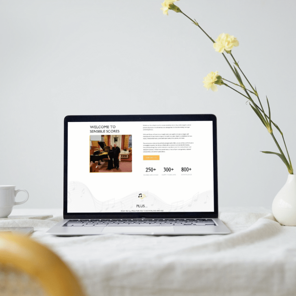 A laptop on a white table displays a website by Moonlit Media. Next to the laptop are a cup, a teapot, and a vase with yellow flowers. The bright, minimal background highlights creative web design services.