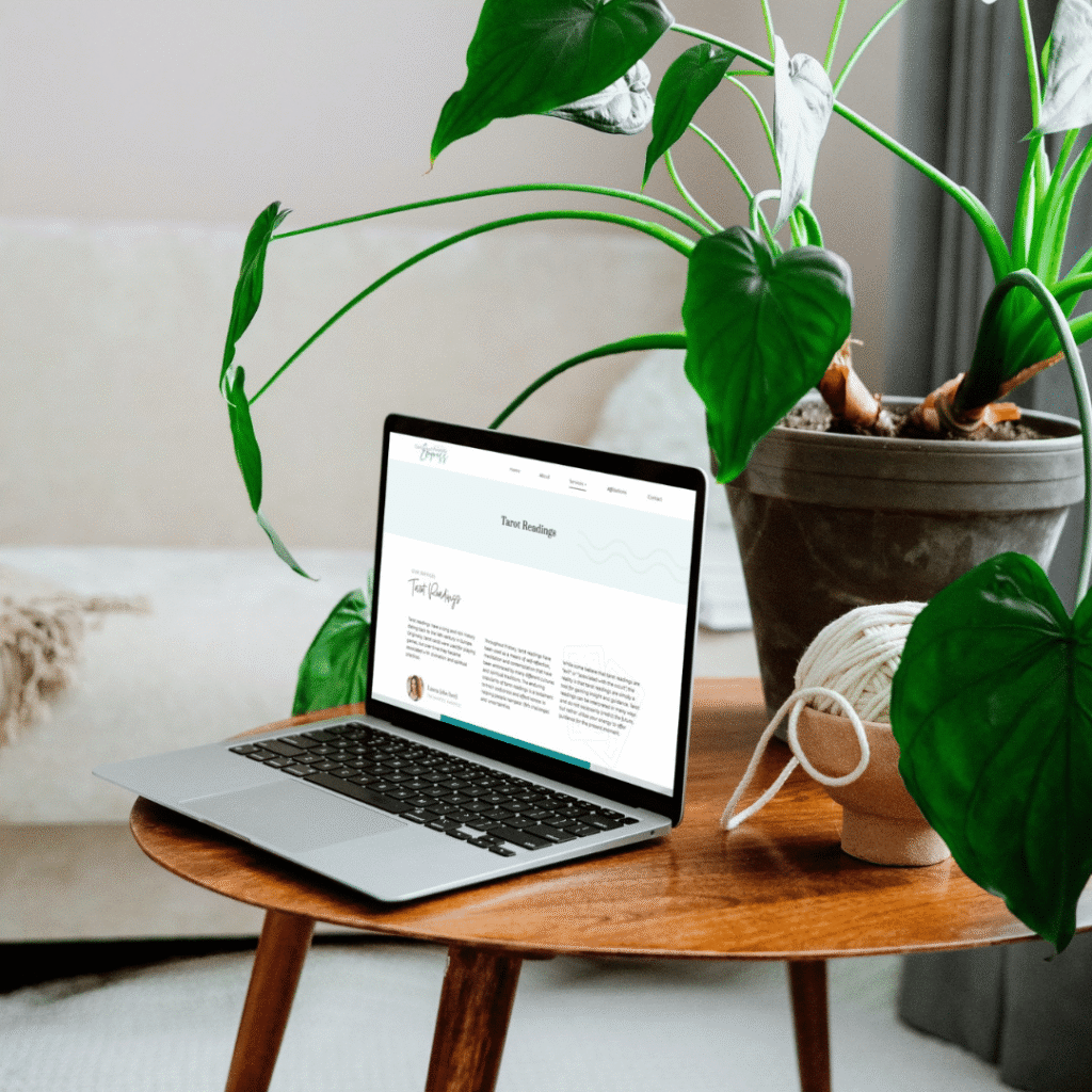 277 | Moonlit Media LLC A laptop showcasing custom website design is placed on a wooden table next to a large potted plant and a ball of string, with a sofa and light-colored wall in the background.