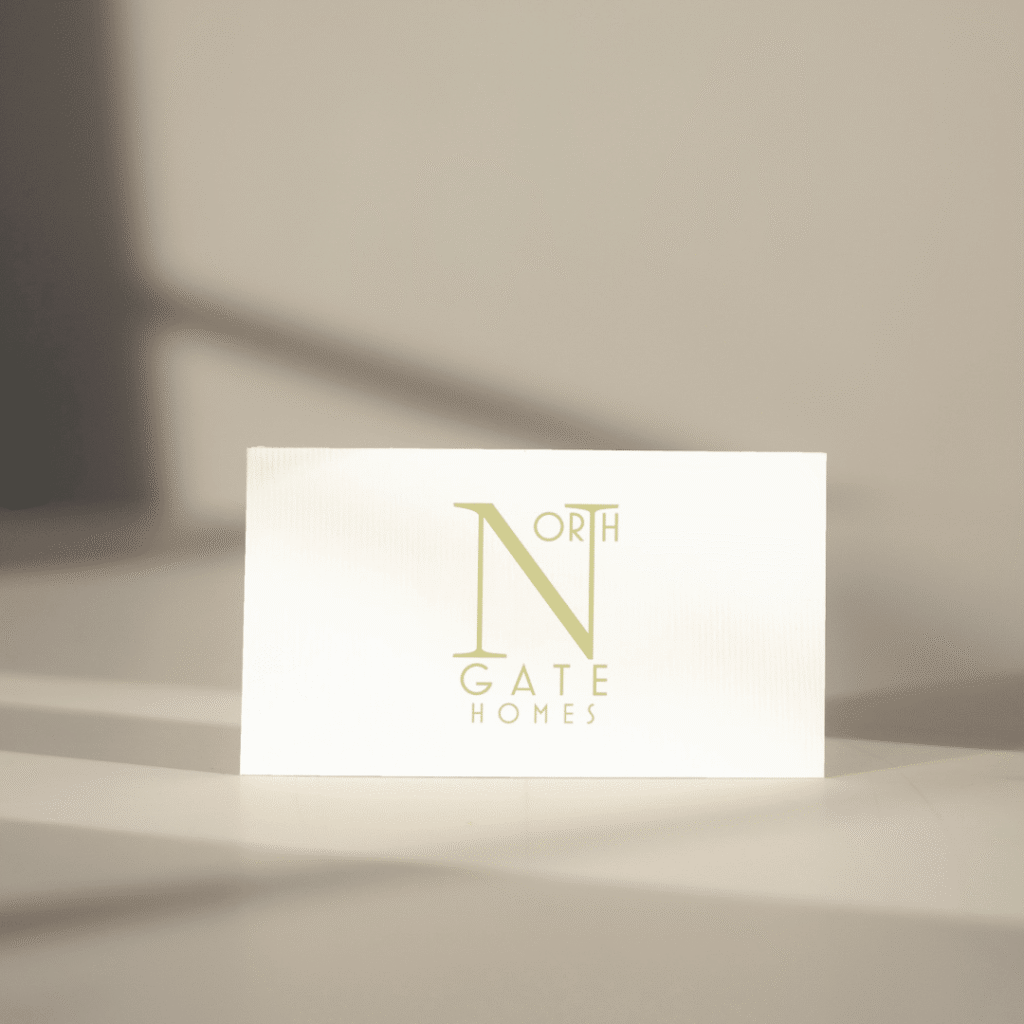 A white card with the NORTH GATE HOMES logo and text in light green, placed upright on a light surface with soft shadows—an elegant example of custom website design by Moonlit Media.