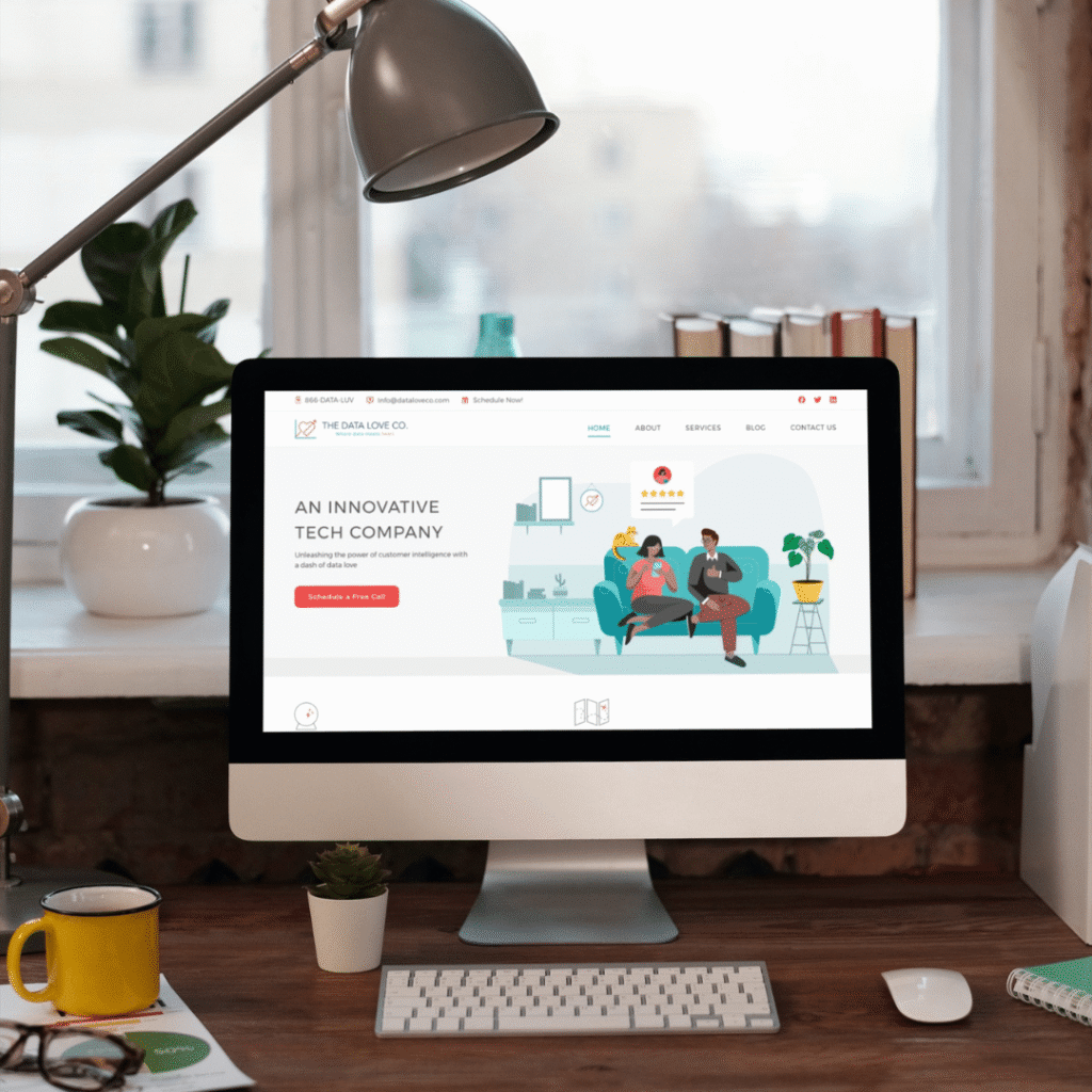 A desktop computer on a home office desk displays a tech company website featuring illustrated people, highlighting custom logo design and web design services. The workspace includes a lamp, potted plants, cups, notepad, and a window in the background.