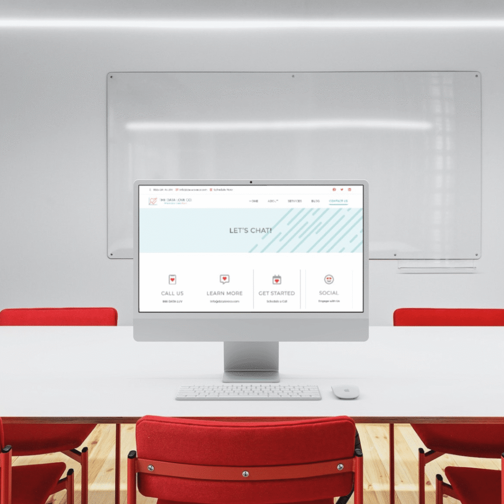 A computer on a white desk in a modern conference room with red chairs and a large whiteboard. The screen showcases Moonlit Media’s web design services, offering contact details and custom logo design options.