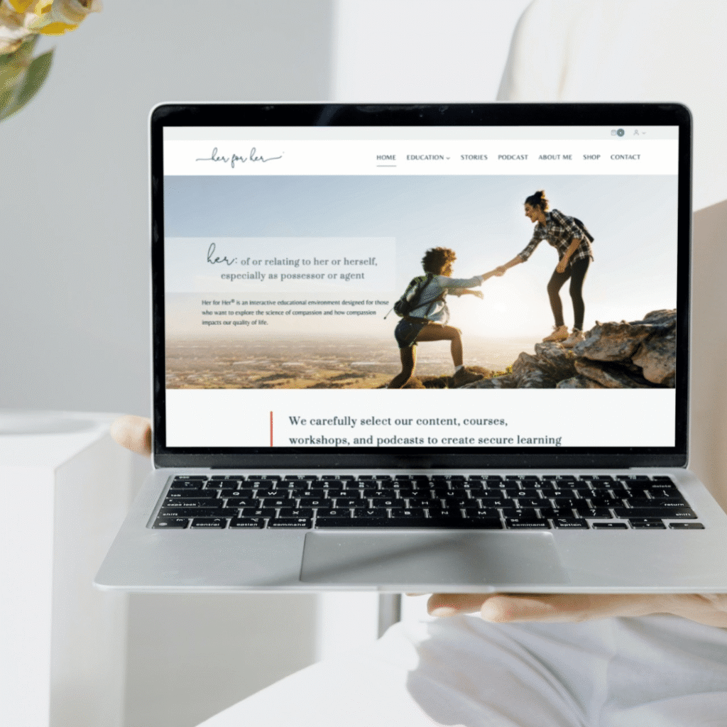 A person holds a laptop displaying a custom website design featuring an image of two people climbing rocks, one helping the other up. The site highlights a definition of her and includes curated educational content below.