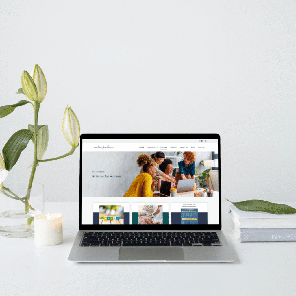 A laptop on a white desk displays a website with women collaborating. The desk also has a green plant, a lit candle, a pen, and stacked books. Discover Moonlit Media’s custom logo design for creative professionals in this minimal, bright scene.