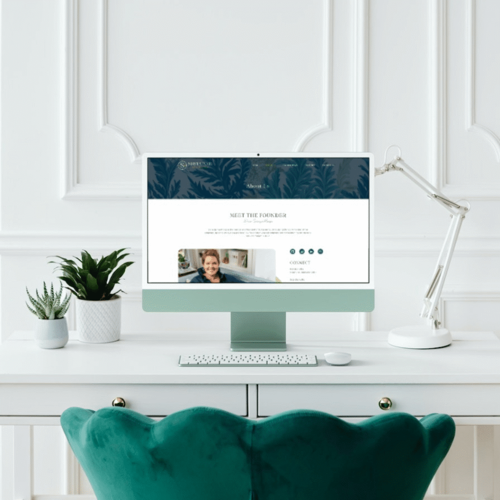 A modern white desk with a green chair, desktop computer, lamp, and small plants. The monitor displays a web designer’s site with a Meet the Founder section and a photo of a smiling person, highlighting custom logo design.