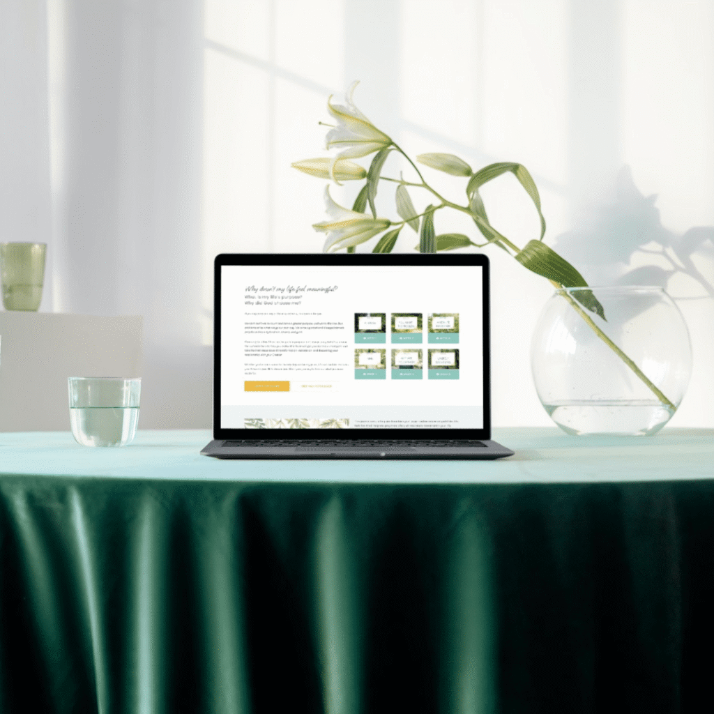 A laptop sits on a green tablecloth next to a round glass vase with a white lily and a glass of water—an inspiring setup for any web designer seeking creative logo design services, bathed in soft natural light through white curtains.