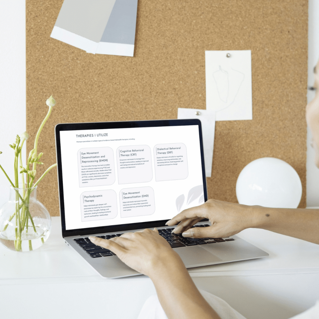 A person types on a laptop displaying a list of therapy types, sitting at a white desk with a vase of flowers, in front of a corkboard with notes—a web designer planning custom website design ideas.