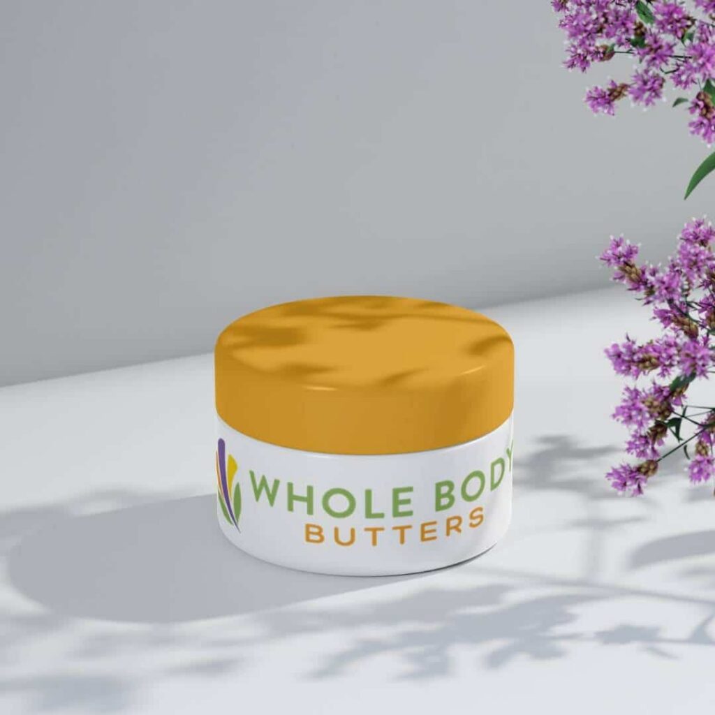 A white jar with a yellow lid labeled Whole Body Butters sits on a white surface. Purple flowers and their shadows are in the upper right, showcasing elegant branding that could inspire your next custom logo design by Moonlit Media.