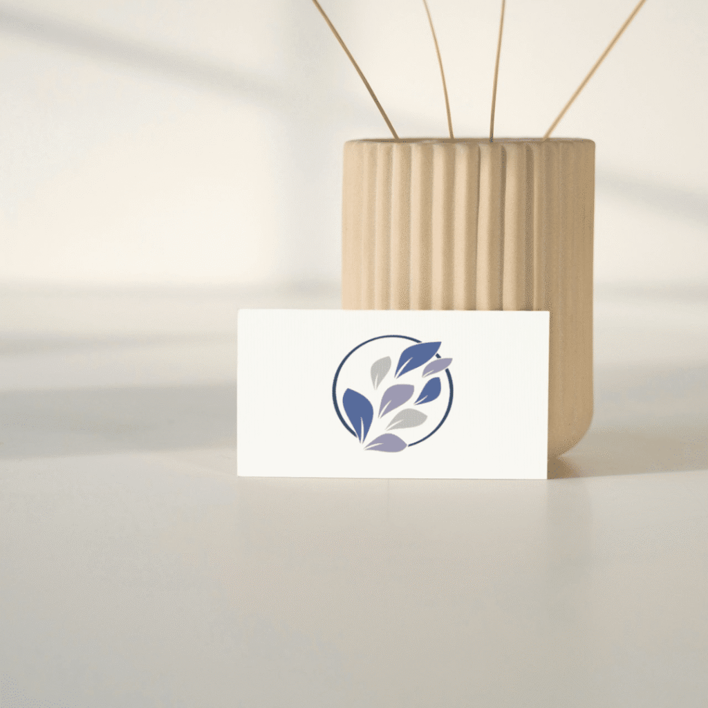 A minimalist business card featuring a blue and gray leaf logo, created through custom logo design, stands in front of a tall, beige, ribbed vase on a white surface with soft lighting.