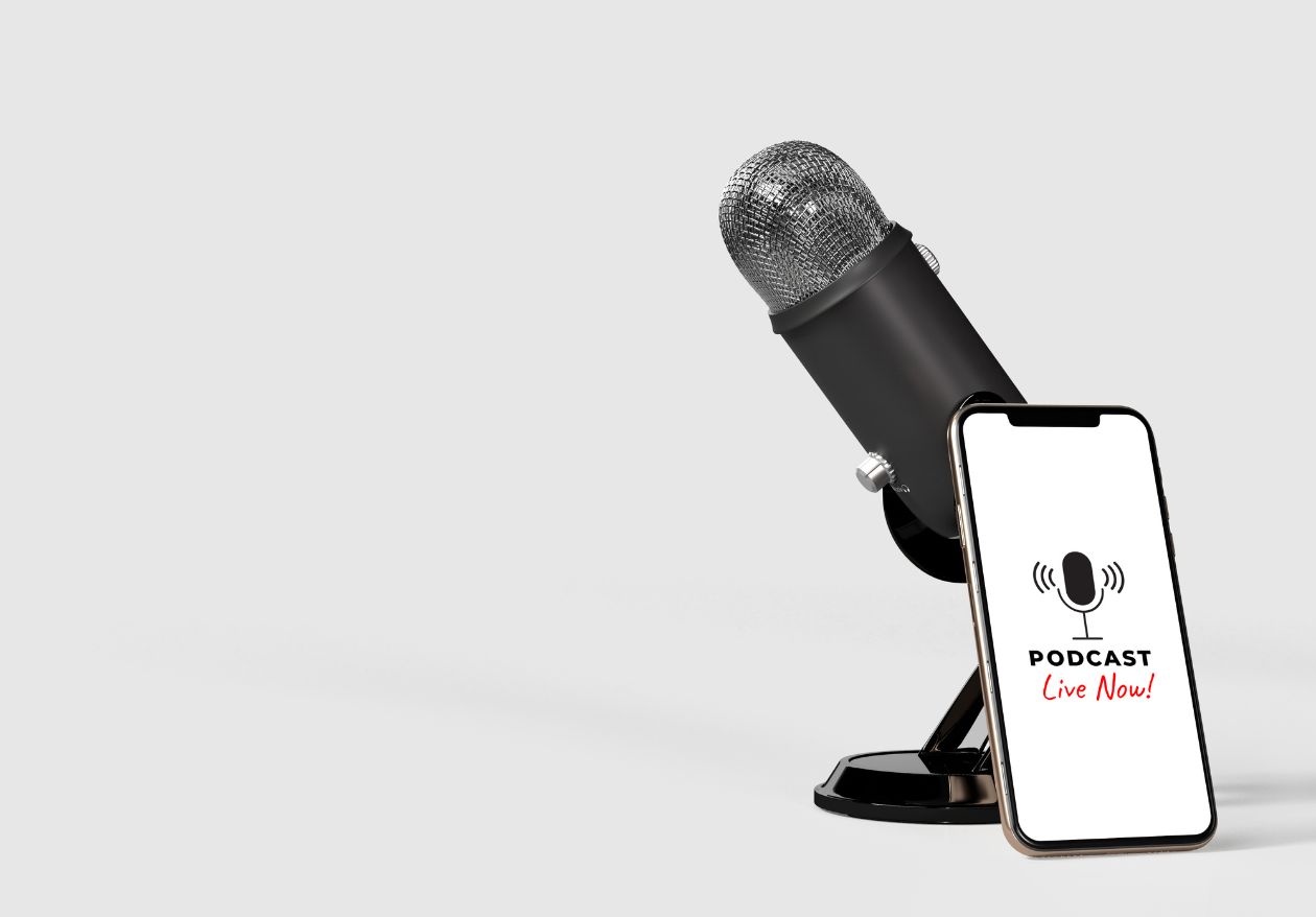 A black microphone on a stand sits next to a smartphone displaying a PODCAST Live Now! screen with a microphone icon, highlighting Moonlit Media’s custom logo design, against a plain light gray background.