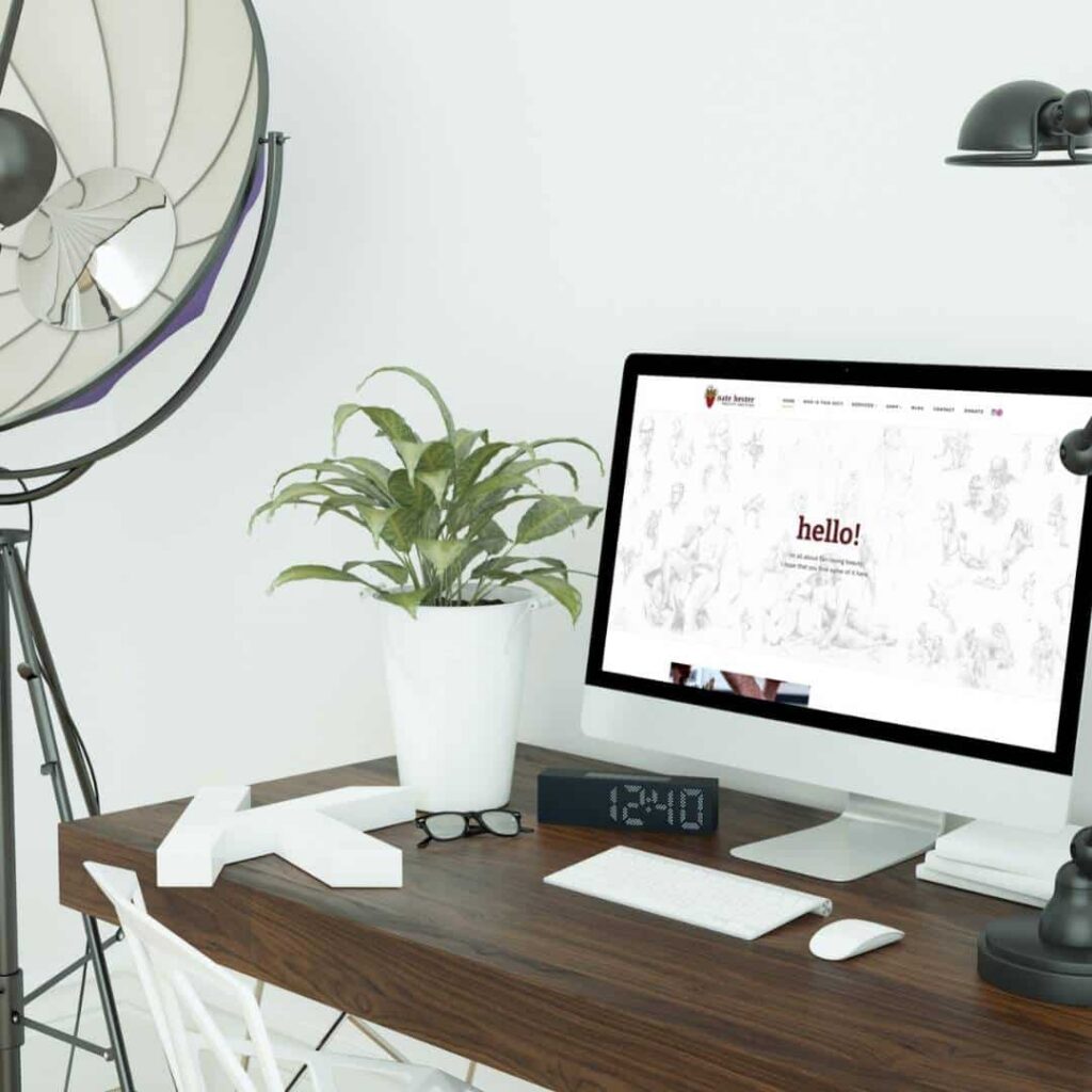 A modern desk setup for a web designer with a computer, large potted plant, black desk lamp, eyeglasses, alarm clock, and white chair. A tripod floor lamp stands nearby, and a custom website design is displayed on the monitor.