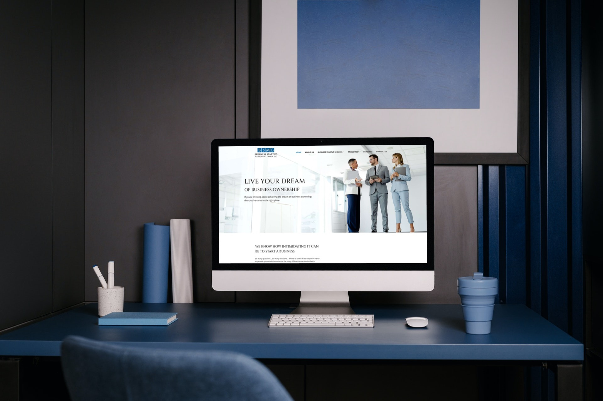 A modern workspace with a blue desk, computer, office supplies, a cup with lid, and a website about Moonlit Media’s web design services displayed on the monitor. Blue wall art and striped panels are in the background.