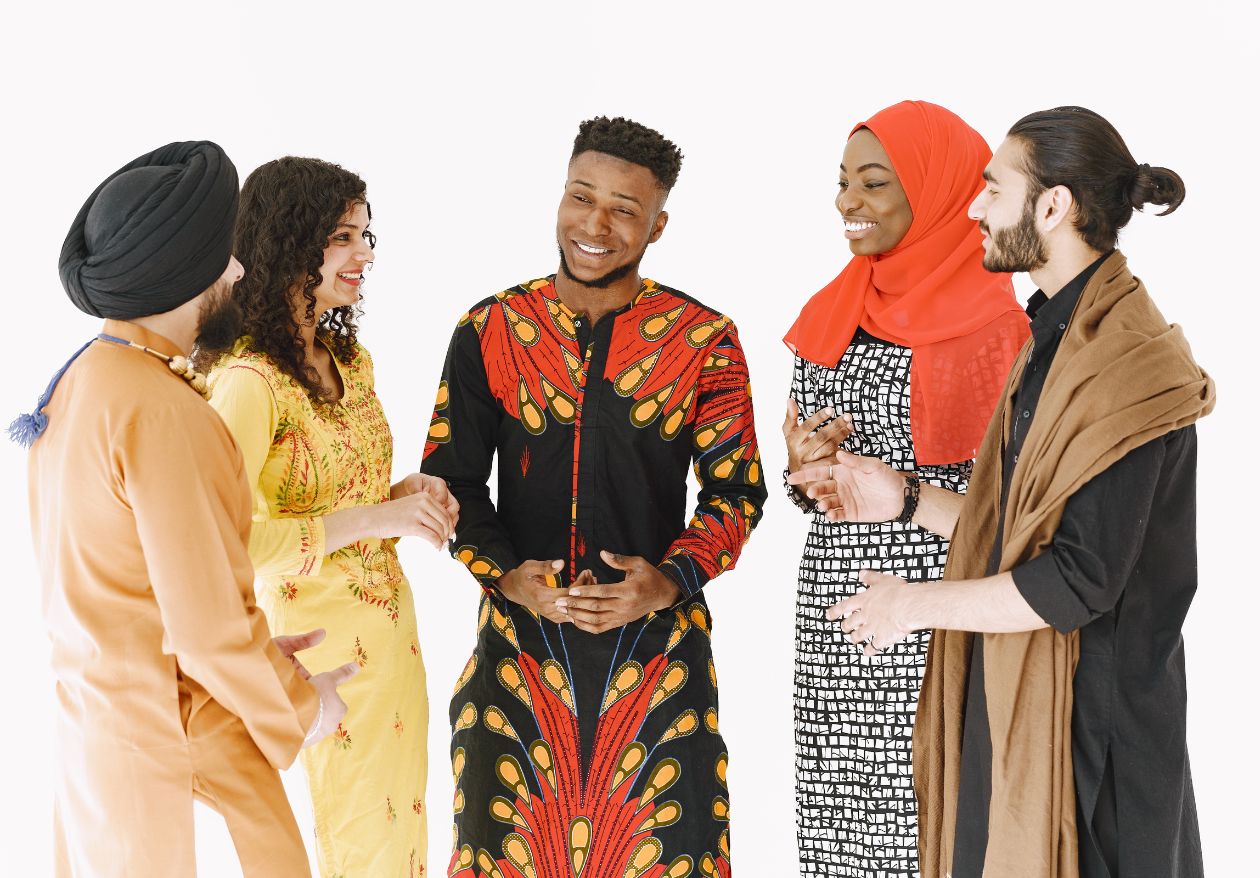 Five people of diverse backgrounds stand in a circle, smiling and talking. Their colorful, traditional clothing reflects various cultures—much like how expert web design services blend diversity and creativity against a plain white background.