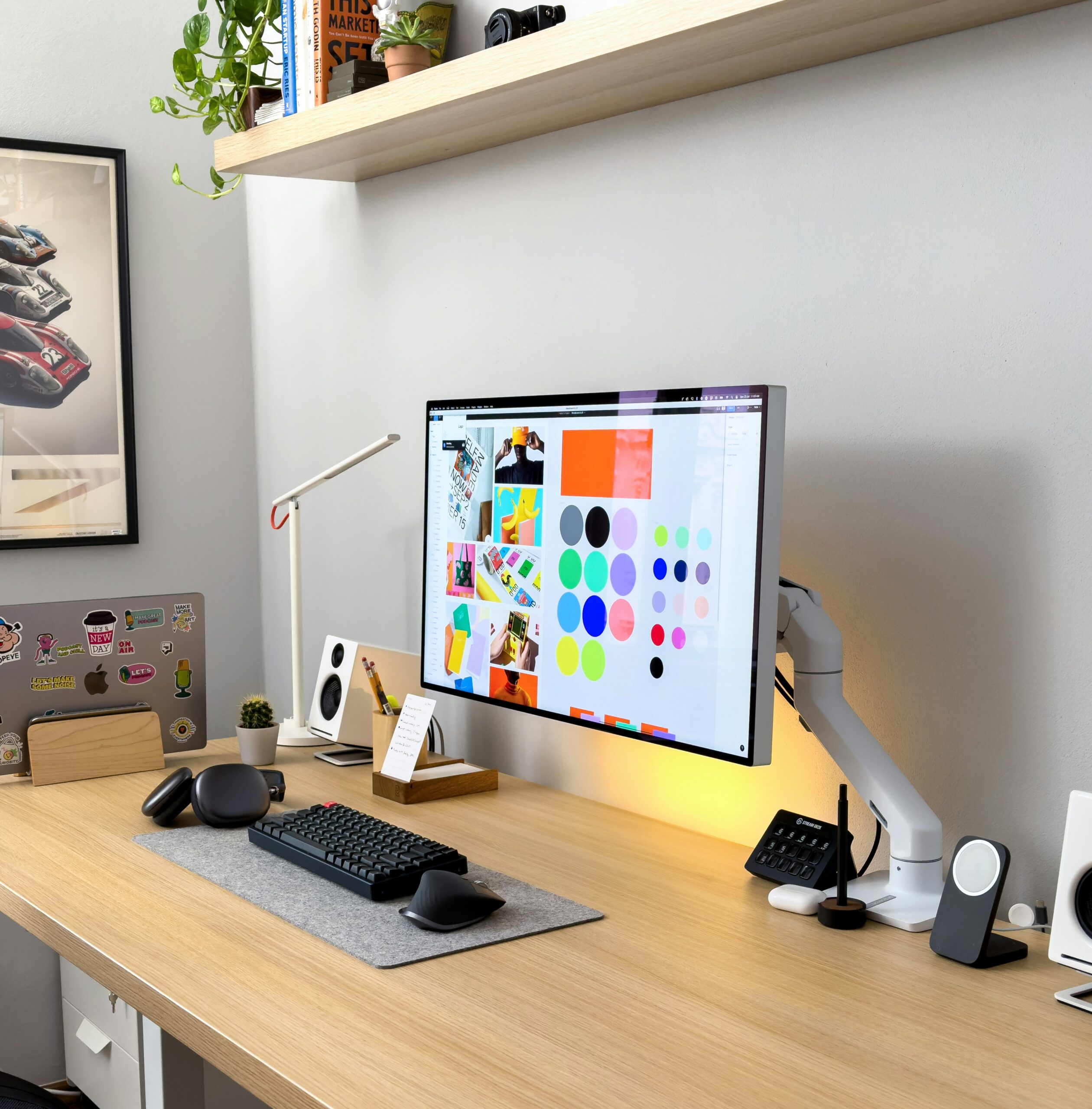 A picture of a desk featuring headphones, speakers, a laptop, and a desktop that's screen shows a graphic design branding board.