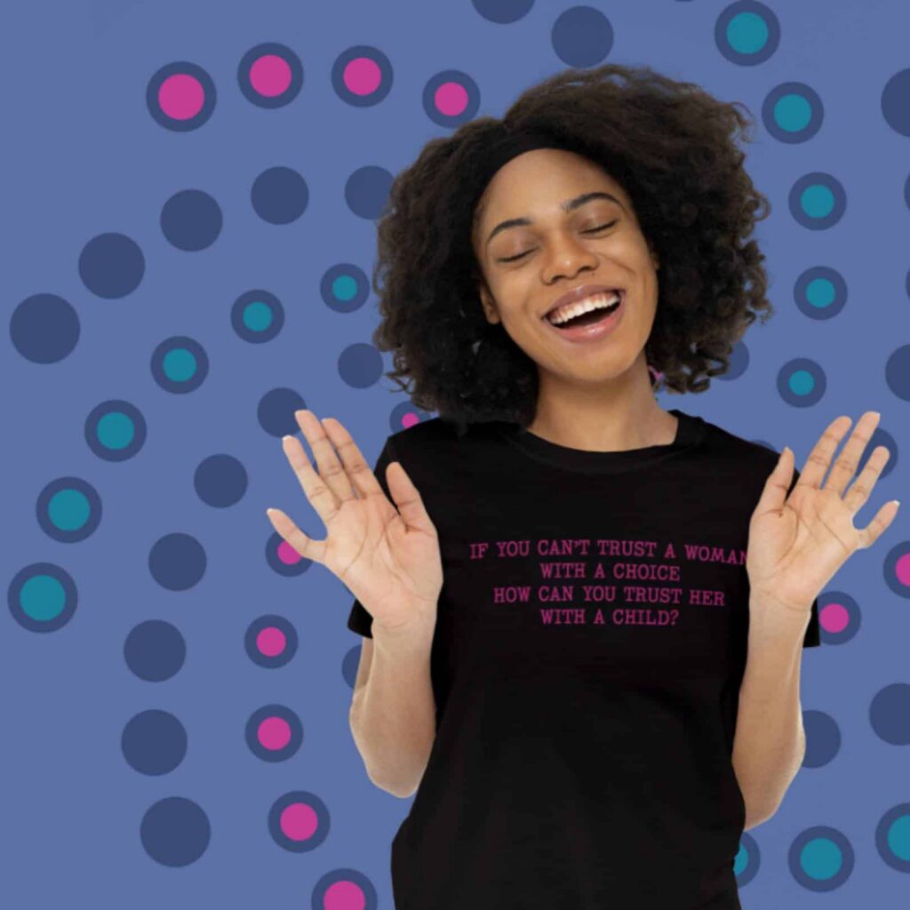A smiling woman stands with her eyes closed and hands raised, wearing a black shirt with pink text. The blue polka dot background brings a modern touch—perfect inspiration for logo design services or custom website design by Moonlit Media.