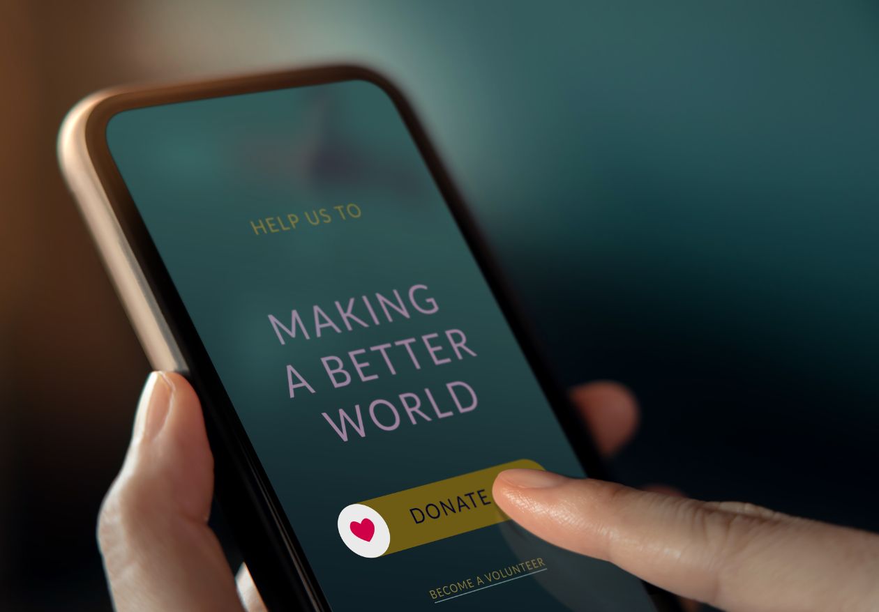 A person holds a smartphone displaying a screen with the text Help us to making a better world and a Donate button with a heart icon, highlighting a charitable initiative by Moonlit Media, known for logo design services and custom website design.